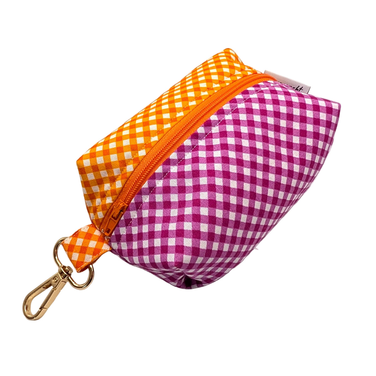 A small zippered pouch with a gingham pattern, featuring orange and white check on one half and magenta and white check on the other, with a gold-tone clip.