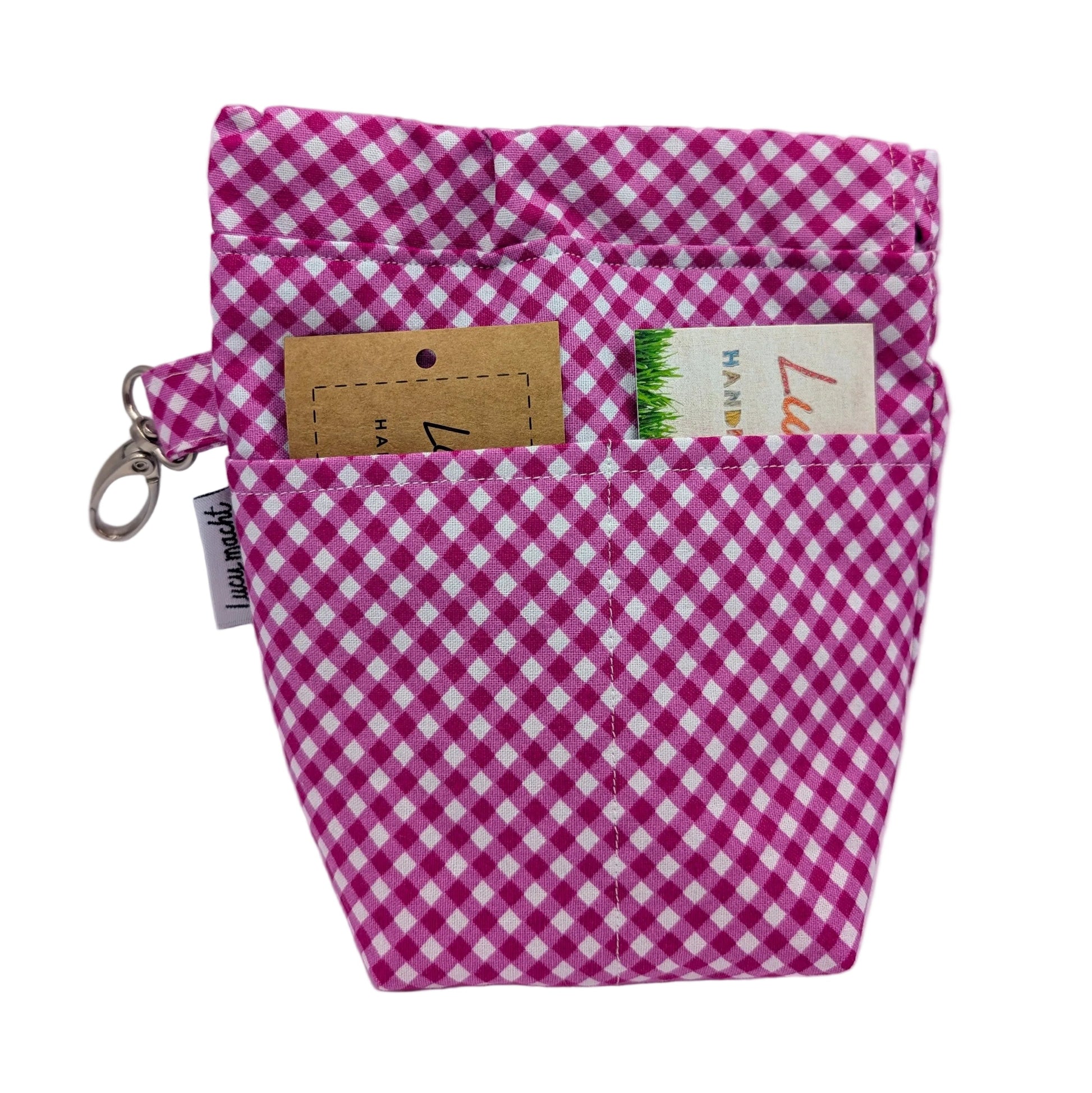 A pink and white gingham fabric pouch with a silver key ring clasp on the left, featuring two front pockets. 